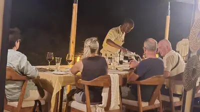 a group of people sitting at a table with a man pouring wine at Tarangire Greenland Retreat in Kaiti