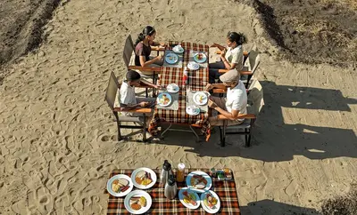 a group of people sitting at a table on the beach at Tarangire Greenland Retreat in Kaiti