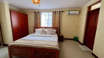 a bedroom with a bed with white sheets and a window at Runako Lodge in Arusha