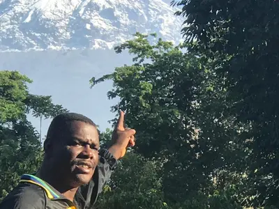 a man with his index finger up in front of a mountain at Lufo Heritage Farm - Octavian Mshiu Residence in Uru