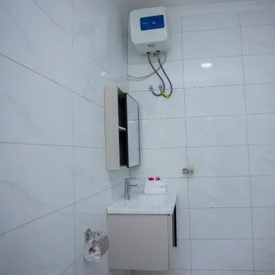a white bathroom with a toilet and a tv on the wall at Enamour Moshi in Moshi