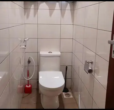 a bathroom with a white toilet and a red brush at QD Apartment in Arusha