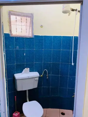 a blue tiled bathroom with a toilet and a window at Kilimanjaroo Inn in Moshi
