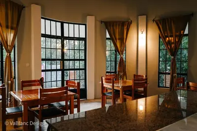 a dining room with tables and chairs and large windows at Naishika Home Stay in Tengeru