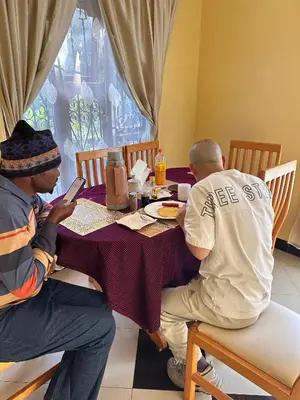 two men sitting at a table looking at their cell phones at J&T Homestay in Karatu