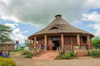 a building with a thatched roof with people standing outside at Naramatisho Women's Centre in Makuyuni
