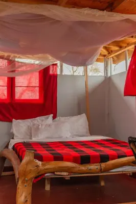 a wooden bed with a red and black checkered blanket at Naramatisho Women's Centre in Makuyuni