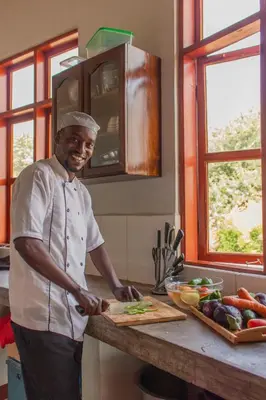 a man standing in a kitchen preparing food on a cutting board at Naramatisho Women's Centre in Makuyuni