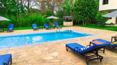 a swimming pool with blue lounge chairs and umbrellas at Sunset Retreat Hotel in Arusha
