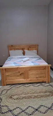 a wooden bed in a bedroom with a rug at African Royal Homestay karatu in Karatu