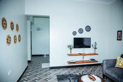 a living room with a couch and a tv on a wall at FM Moshono Apartment in Arusha