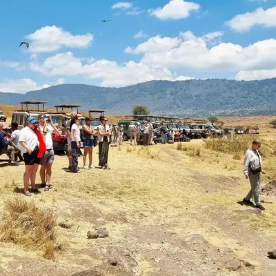 a group of people standing in a field with vehicles at Summit Scape Adventures Safaris Limited in Arusha