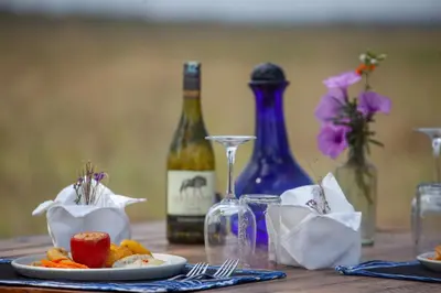 a table with a bottle of wine and a plate of food at Mawe Tented Camp in Serengeti