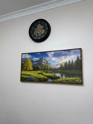 a clock hanging on a wall with a painting of a mountain at Oasis Residence in Arusha