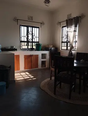 a living room with a table and two windows at Zebra Homestay in Mto wa Mbu