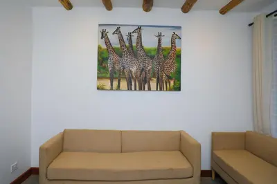 a living room with a couch and a painting of giraffes at Heart Of Africa Lodge Acacia in Mkulat