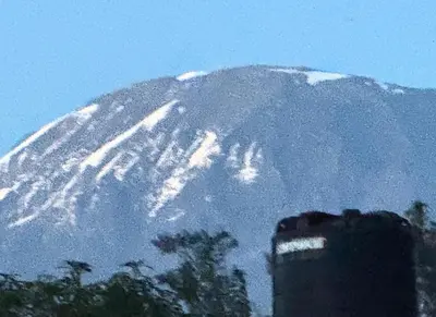 a snow covered mountain in front of a building at Bibi Cosy Cottage in Moshi