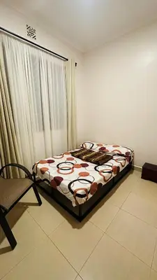 a bedroom with a bed and a chair and a window at Small White House Njiro in Arusha