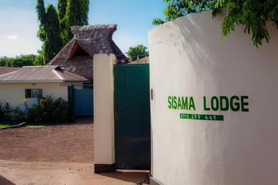 a white wall with a santa lodge sign on it at Sisama Lodge in Msaranga