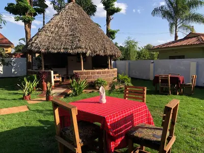 a table and chairs with a table and a thatch hut at Sisama Lodge in Msaranga