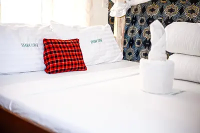 a bed with white pillows and a red checked pillow at Sisama Lodge in Msaranga