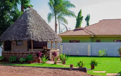 a small hut with a thatched roof in front of a house at Sisama Lodge in Msaranga