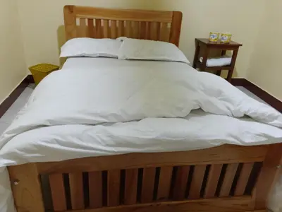 a large wooden bed with white sheets and pillows at Moshi Roots Homestay in Msaranga