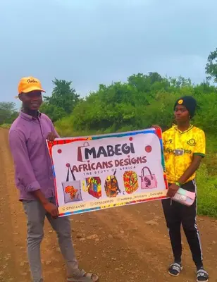 two people holding a sign on a dirt road at Mabegi african Designs in Arusha