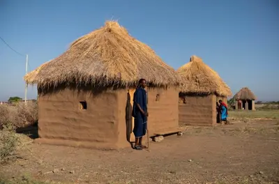 a man is standing in front of a thatched hut at Ewang'ani Maasai Cultural Village - Overnight Experience and Tour in Sanya Chini Station
