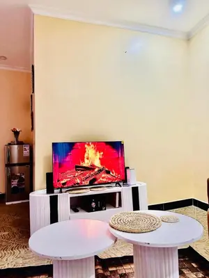 a living room with two tables and a flat screen tv at Cozy 1Bedroom Stand Alone -Near Clock Tower Arusha in Arusha