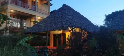 a house with a thatched roof in front of a building at Camp Kimanganu Safari Lodge in Msaranga