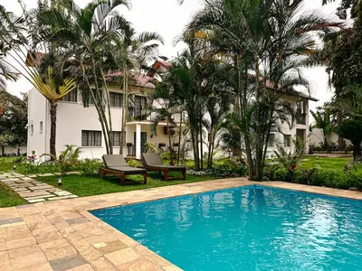a swimming pool in front of a house with palm trees at Brubru Lodge in Moshi