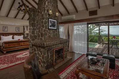 a living room with a stone fireplace and a bed at Ngorongoro Oldeani Mountain Lodge in Oldeani