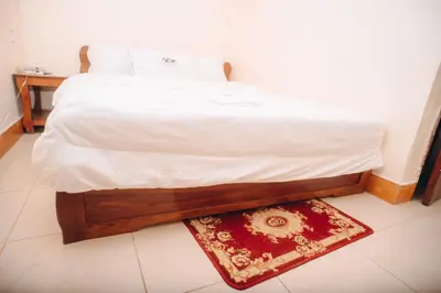 a bedroom with a bed with white sheets and a rug at Arusha Giraffe Lodge in Arusha