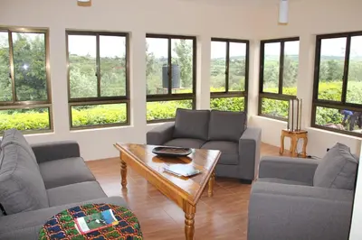 a living room with couches and a table and windows at Tanzanice Farm Lodge in Karatu