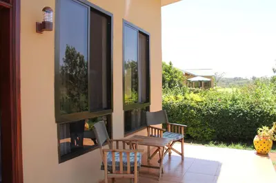 a patio with three windows and a table and chairs at Tanzanice Farm Lodge in Karatu