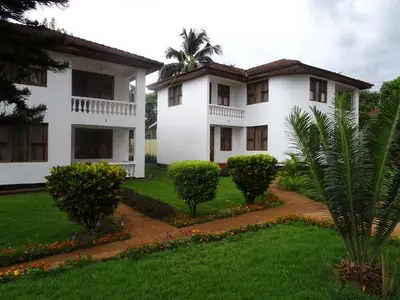 a white house with trees and a green yard at Keys Hotel Mbokomu Branch in Moshi