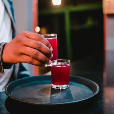 a person holding two glasses of red drink on a table at Crest Safari Lodge Bed and Breakfast in Arusha