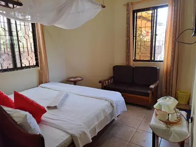a bedroom with two beds and a chair and windows at Rainbow Executive Lodge in Boma la Ngombe