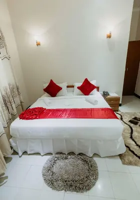 a bedroom with a large white bed with red pillows at Panama Garden Resort in Moshi
