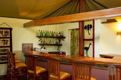 a bar with chairs and a counter with alcohol bottles at Mbuzi Mawe Serena Camp in Serengeti