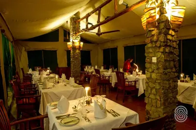 a dining room with white tables and a woman in the background at Mbuzi Mawe Serena Camp in Serengeti