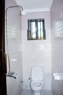 a white bathroom with a toilet and a window at Wanyama B&B in Arusha