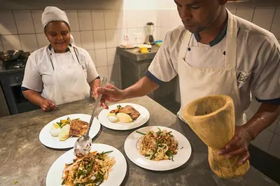 two people in a kitchen preparing plates of food at Arusha Villa Karamu Coffee Estate in Usa River