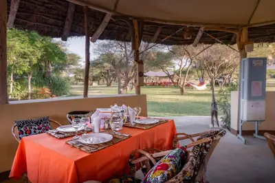 a table with orange table cloth and chairs with a view of a park at Lake Natron Maasai giraffe eco Lodge and camping in Mtowabaga