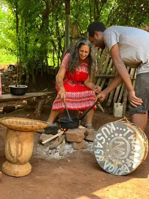 a man and a woman sitting on a bench cooking over a fire at Shimbwe Meadows Home in Moshi