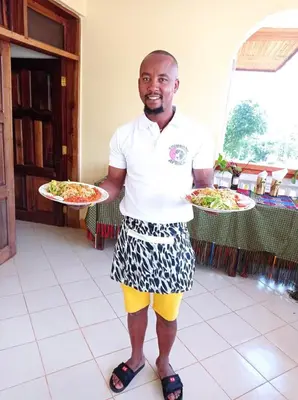 a man is holding two plates of food at Shimbwe Meadows Home in Moshi
