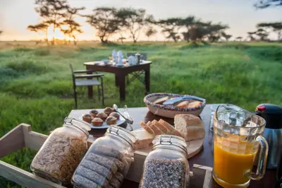 a picnic table with bread and glasses of orange juice at Serengeti Sametu Camp in Serengeti National Park