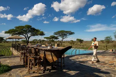 a man walking by a table with a pool at Serengeti Sametu Camp in Serengeti National Park