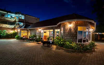 a woman sitting on a bench outside of a building at night at Mrimba Palm Hotel in Arusha